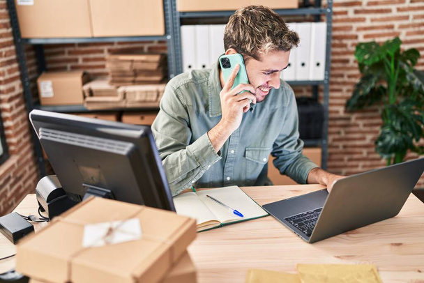 Jongeman e-commerce zakenman met behulp van laptop praten op smartphone op kantoor - Foto, afbeelding