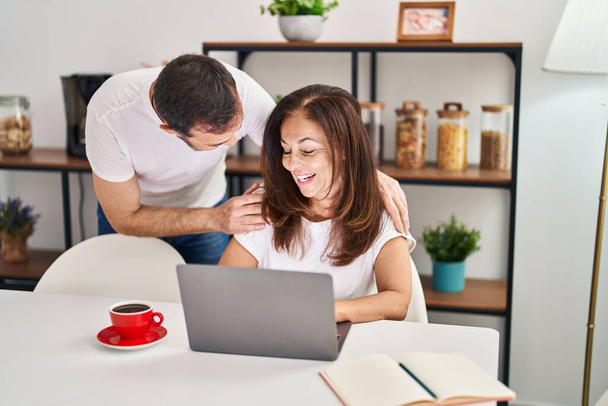 Middle age man and woman couple hugging each other working sitting on table at home - Foto, Imagem