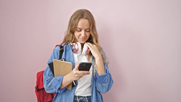 Young blonde woman student holding books using smartphone with doubt expression over isolated pink background - Foto, afbeelding