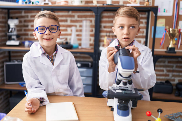 Adorable boys students using microscope writing notes at laboratory classroom - Фото, изображение