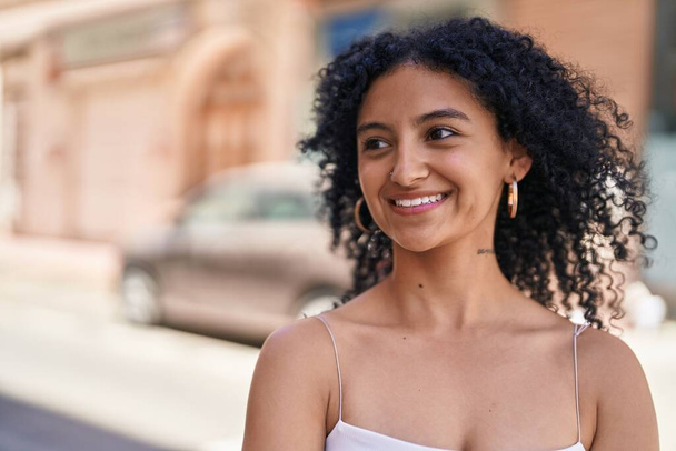 Молода іспаномовна жінка посміхається впевнено дивлячись в бік на вулиці
 - Фото, зображення