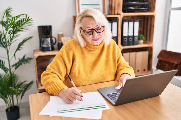 Moyen-âge blonde femme d'affaires écriture sur le document de travail au bureau - Photo, image
