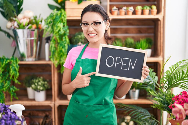 Hispanic young woman working at florist holding open sign smiling happy pointing with hand and finger  - Photo, Image