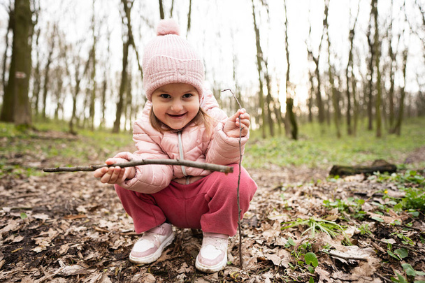 Baby girl playing with sticks in spring forest.  - Фото, изображение