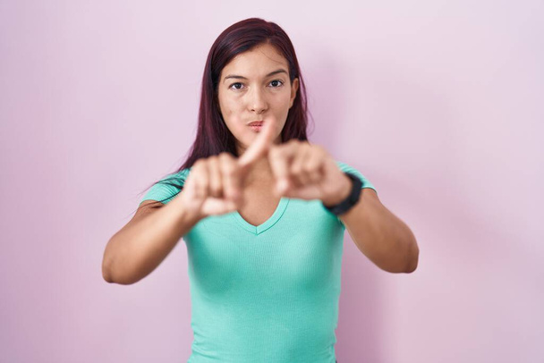 Young hispanic woman standing over pink background rejection expression crossing fingers doing negative sign  - Foto, imagen