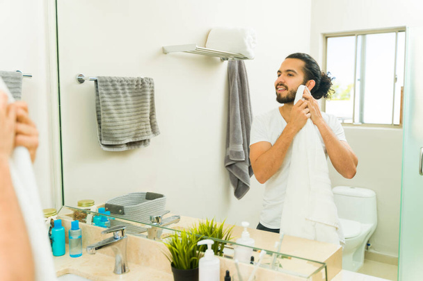 gelukkig aantrekkelijke jongeman drogen zijn baard na wassen en verzorgen tijdens zijn ochtend routine - Foto, afbeelding