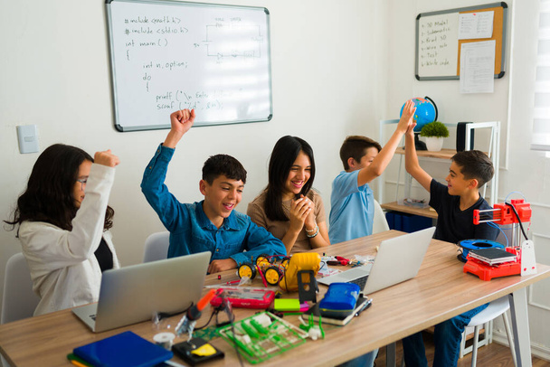 Podekscytowani młodzi nastolatkowie śmiejący się i świętujący podczas zabawy programowania i korzystania z robotów elektronicznych w klasie - Zdjęcie, obraz