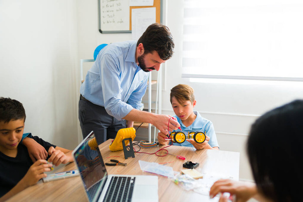 Robotiklehrer hilft einem Teenager-Schüler beim Bau eines elektronischen Prototypen, während er während eines Bildungskurses programmiert - Foto, Bild