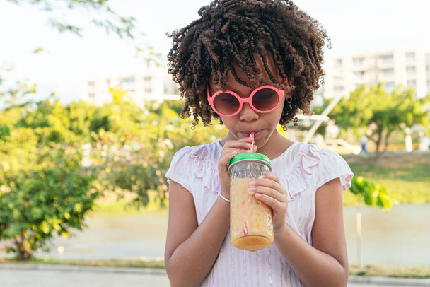 Mädchen mit lockigem Haar bei einem gesunden Drink im Park - Foto, Bild