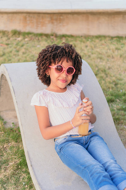 Κορίτσι κάθεται σε ένα παγκάκι στο πάρκο πίνοντας χυμό - Φωτογραφία, εικόνα