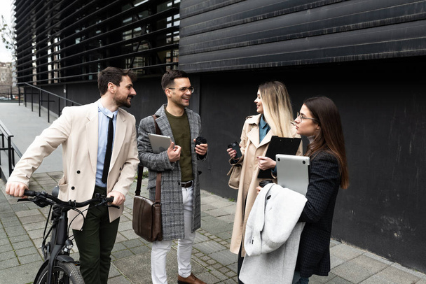 Quick briefing before meeting. Group of cheerful young successful business people talking to each other while walking outdoors. Office workers experts exchanging ideas - 写真・画像
