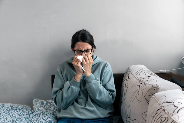 Ill upset young woman sitting on sofa covered with blanket freezing blowing running nose got fever caught cold sneezing in tissue, sick girl having influenza symptoms coughing at home, flu concept - Foto, immagini