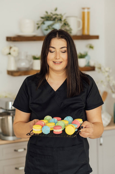 Woman confectioner holding traditional french colorful macarons in a rows on a metal mesh. - Foto, afbeelding