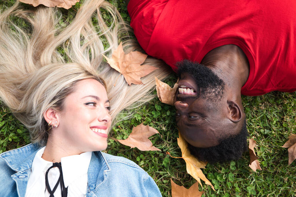 Happy interracial couple lying on the grass. Couple looks at each other with happiness. - Foto, afbeelding