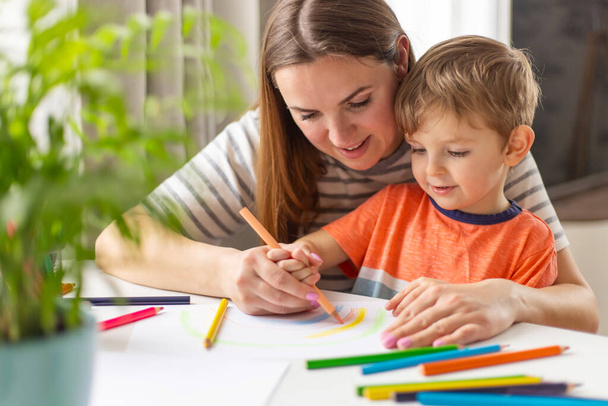 Dessin de la mère et de l'enfant avec des crayons assis au bureau à la maison. Famille heureuse - Photo, image