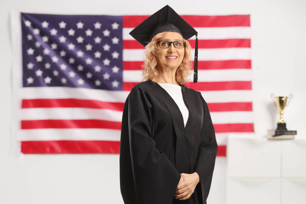 Marture nainen yllään valmistunut puku ja poseeraa edessä USA lippu - Valokuva, kuva