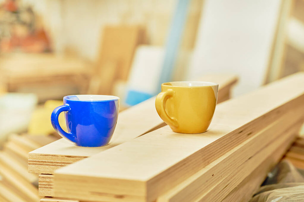  Work break, tea coffee time. Blue and yellow cups in carpentry on wooden planks                               - 写真・画像