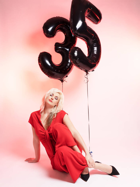 Mooi blond in rode avondjurk en ballonnen 35. Hij viert zijn verjaardag. Roze achtergrond. - Foto, afbeelding