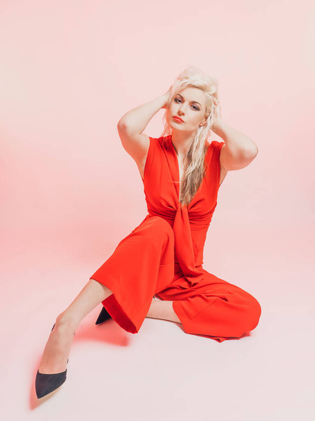 Porträt einer schönen blonden Frau in einem roten Strumpfanzug.. Posieren im Studio auf rosa Hintergrund. - Foto, Bild