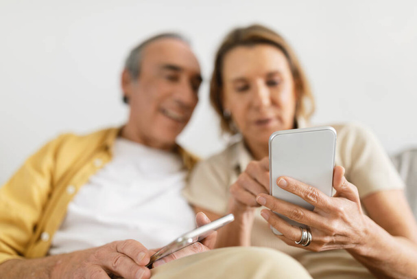 Casado pareja de personas mayores utilizando teléfonos inteligentes, tratando de entender la aplicación móvil, navegar por Internet, enfoque selectivo, primer plano. Generación más antigua usando gadget inalámbrico - Foto, imagen