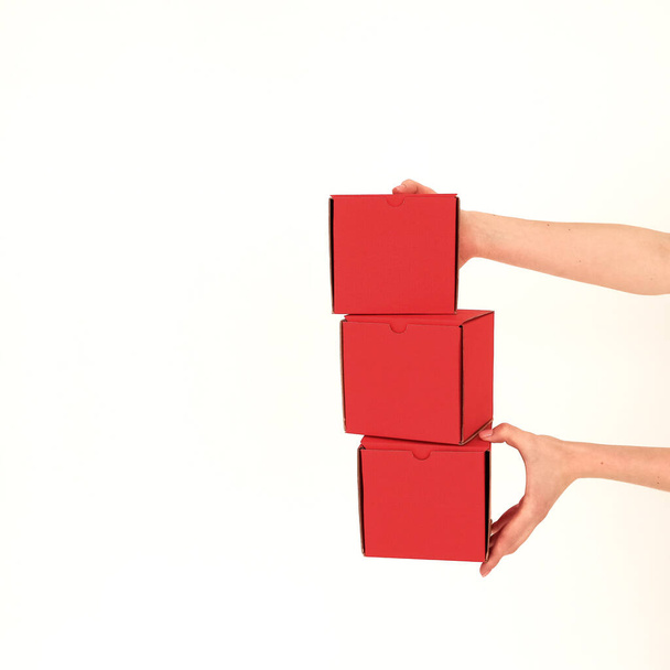 Red square craft boxes hold human hands on a white background. Place for text and logo. The concept of the holiday, packaging, gifts. High quality photo - 写真・画像