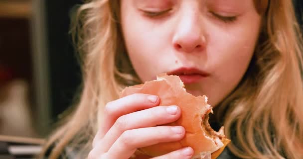 felice ragazza con lunghi capelli biondi mangia un hamburger con piacere. orizzontale - Filmati, video