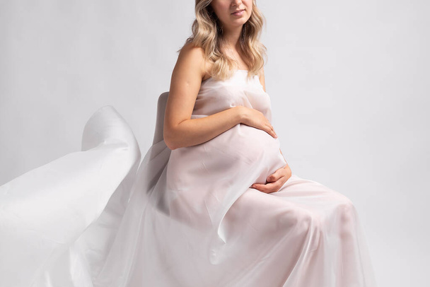 Tyylikäs raskaana oleva nuori nainen seisoo yllään lentävä valkoinen kangas. Raskaus, äitiys ja äitiys. - Valokuva, kuva