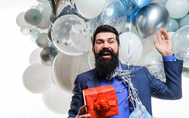 Happy bearded man with helium balloons holds gift box. Smiling man celebrating birthday. Party time. Handsome businessman celebrating something. Festive event. Birthday party. Anniversary. Present - Zdjęcie, obraz