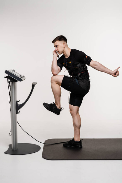 Musculaire mannelijke atleet in EMS pak doet workout sport training die elektrische impulsen gebruikt om spieren op witte achtergrond te stimuleren. Sport training in elektrische spierstimulatie pak - Foto, afbeelding