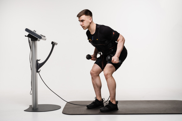 Männliche Sportler mit muskulösem Aufbau trainieren mit dem EMS-Anzug, der elektrische Impulse zur Aktivierung der Muskeln aussendet. Trainer macht Sporttraining mit elektrischem Muskelstimulationsanzug - Foto, Bild
