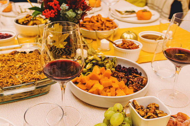 Close-up of the glass with red wine on the Thanksgiving dinner table decorated in warm colors - Фото, изображение