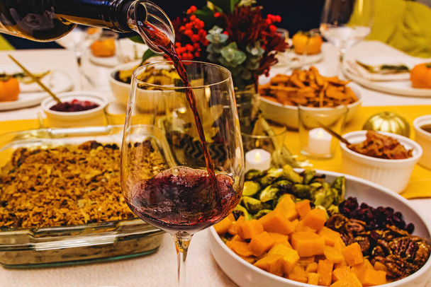 Red wine pouring into a glass standing on Thanksgiving dinner party table, close-up - Foto, imagen
