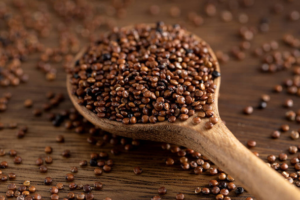 Főzetlen vörös quinoa magok fakanál. Quinoa mag elterjedt rusztikus háttérrel. 45 fokos lövés.. - Fotó, kép