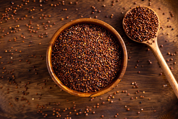 Ongebakken rode quinoa zaden houten lepel. Quinoa zaden verspreid over rustieke achtergrond. Omhoog zicht graden schieten. - Foto, afbeelding