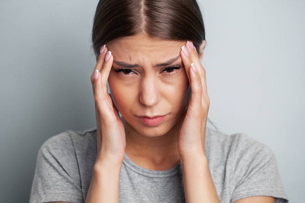 Молодая уставшая женщина чувствует головную боль и держит место боли руками. - Фото, изображение