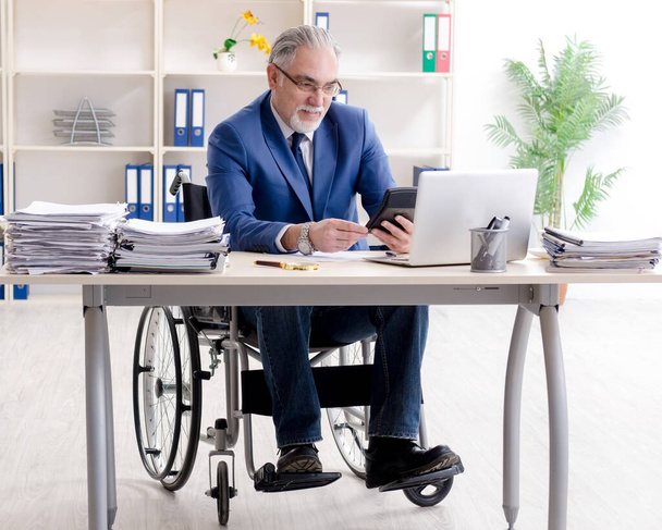 De oudere werknemer in een rolstoel die in het kantoor werkt - Foto, afbeelding