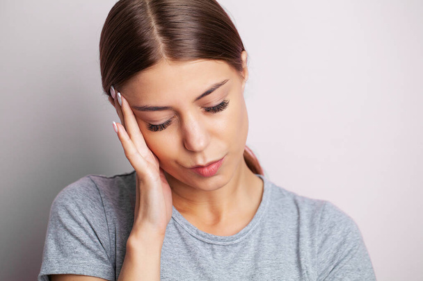 Une jeune femme fatiguée ressent un mal de tête et tient la place de la douleur avec ses mains. - Photo, image