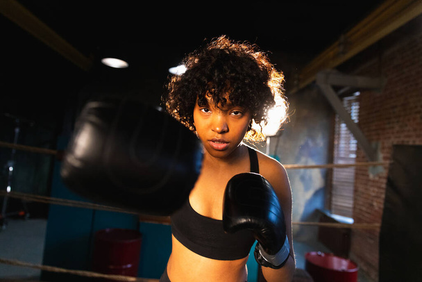 Kobieca samoobrona. Afroamerykanka bokserka uderzająca rękawiczkami bokserskimi do kamery. Zdrowe silne dziewczyny uderzające treningowe ciosy wyglądające na skoncentrowane prosto. Odpowiedni trening ciała - Zdjęcie, obraz