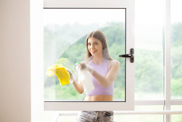 Woman in purple t-shirt cleaning window with cleanser spray and rag. - Foto, Bild