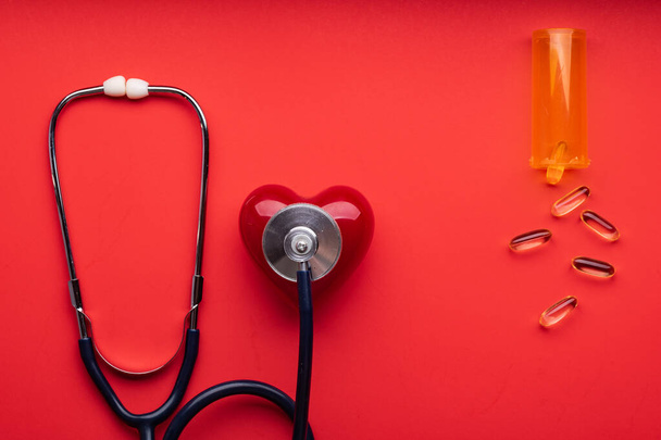 Stethoscope, pills and red heart on red background, top view. Space for text. - Photo, Image