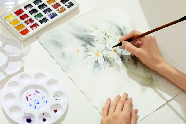 Woman painting flowers with watercolor at white table, above view. Creative artwork - Foto, Imagem