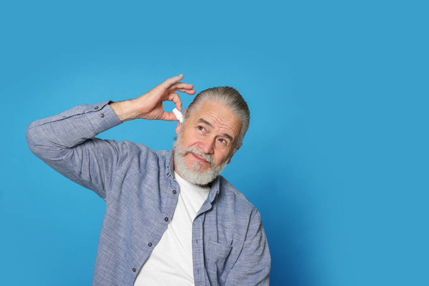 Senior man using ear drops on light blue background, space for text - Foto, Imagem