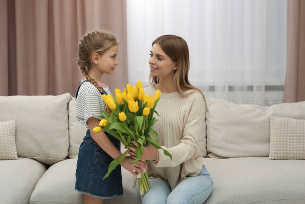 Little daughter congratulating mom with bouquet of yellow tulips at home. Happy Mother's Day - Foto, Imagen