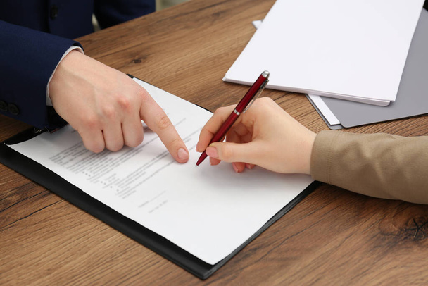 Man pointing at document and woman putting signature at wooden table, closeup - Фото, зображення