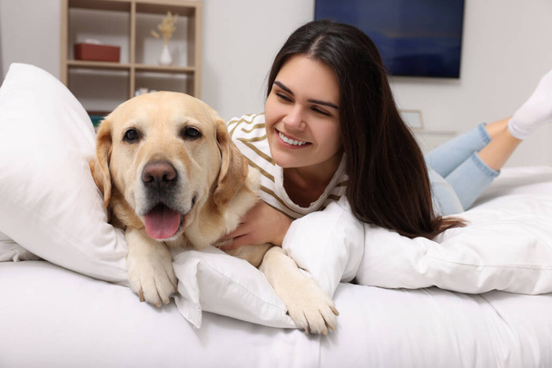 Happy woman with cute Labrador Retriever on bed at home - Foto, Imagem