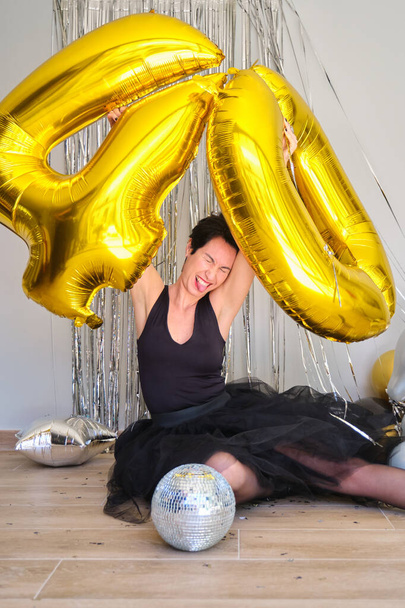 Blanke vrouw in een 40 jarig feest met 40 gouden ballonnen op de vloer. - Foto, afbeelding