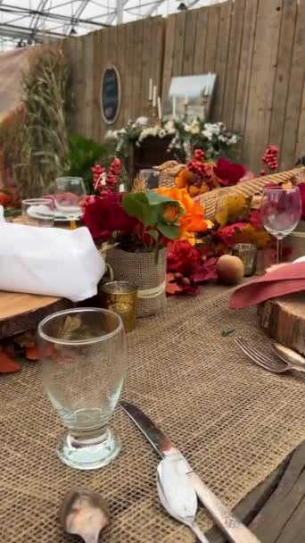 Pöydällä on lautasia puisilla telineillä haarukoiden vieressä veitset ja lasit Kuivat punaiset ja mustat maissinpunaiset lautasliinat keskellä kaikki on valmis päivälliselle Halloween-syksyllä lokakuu-iltana.  - Materiaali, video