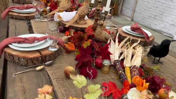 On table there are plates on wooden stands next to forks knives and glasses Dry heads of red and black corn red napkins in middle everything is ready for dinner on Halloween autumn October evening  - Footage, Video