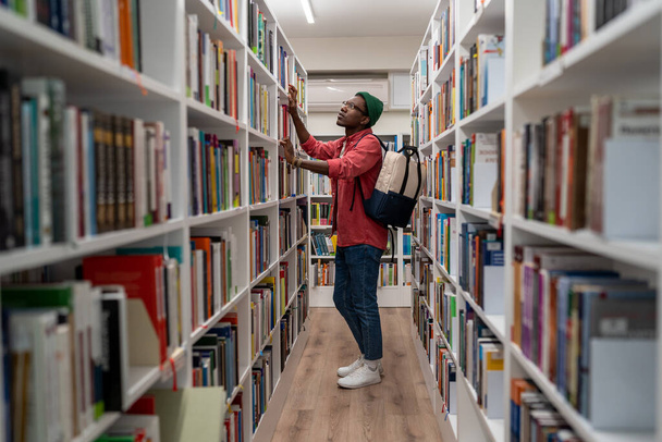 大学図書館で教育研究のための資料を探している思慮深い黒人学生の男。書店で読書のための本を選択する若いアフリカの男、選択的な焦点。文学・教育 - 写真・画像