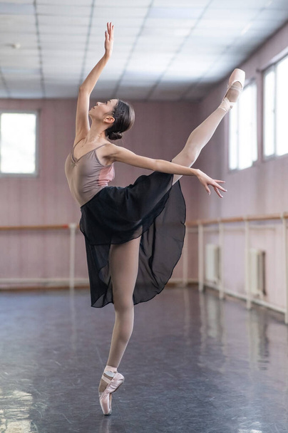 Graceful Asian ballerina in a beige bodysuit and black skirt is rehearsing in a dance class - Zdjęcie, obraz